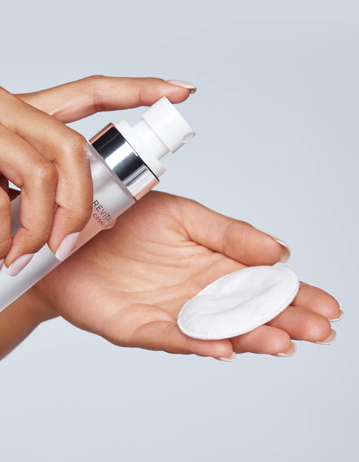 Vor einem hellen Hintergrund sprüht eine Hand die Micellar Water Lash Wash
auf ein Wattepad, das sie in der anderen Hand hält.