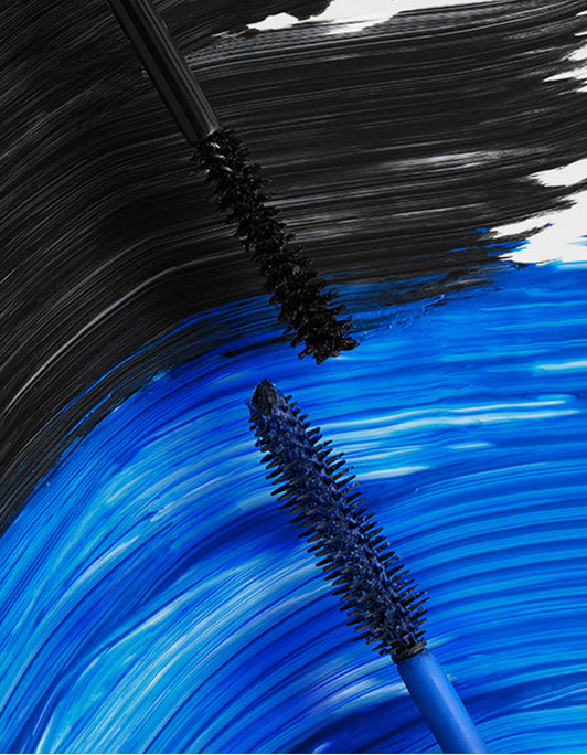 Nahaufnahme der Bürsten des Double-Ended Volume Mascara Set von RevitaLash® Cosmetics in Schwarz und Blau mit passenden Mascara-Strichen im Hintergrund.