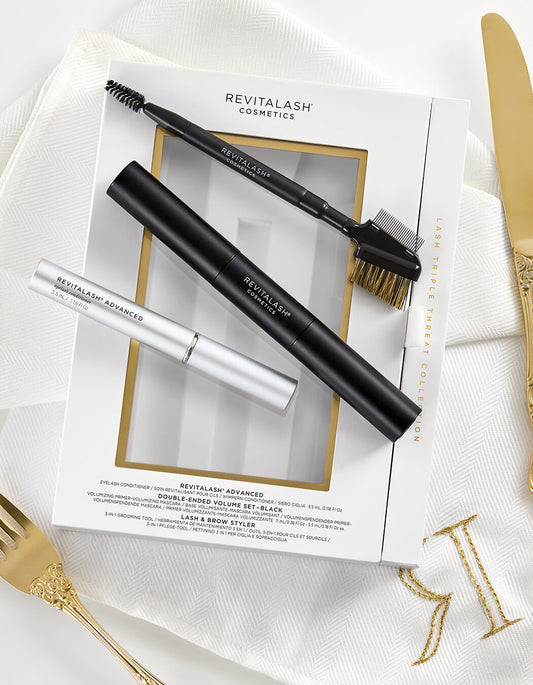RevitaLash Geschenkset mit Mascara, Conditioner und Styling-Tool, elegant präsentiert auf weißem Stoff mit goldenen Besteckdetails.