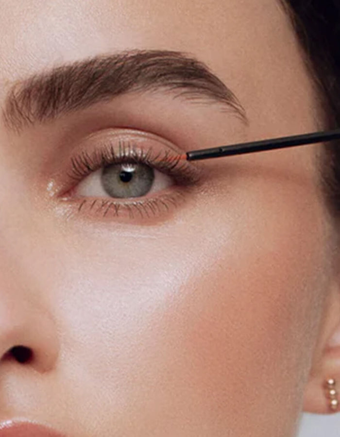 Nahaufnahme einer Frau, die mit dem feinen Applikator ein Wimpernserum präzise am oberen Wimpernkranz aufträgt.