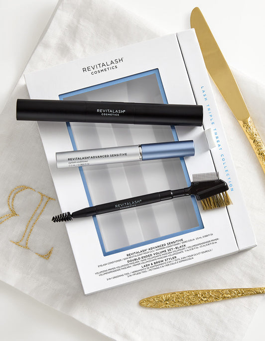 Revitalash Sensitive Lash Triple Threat Collection - RevitaLash® Advanced Sensitive mit Wimpernserum, Mascara und Styling-Bürstchen auf weißer Box, daneben goldenes Besteck.