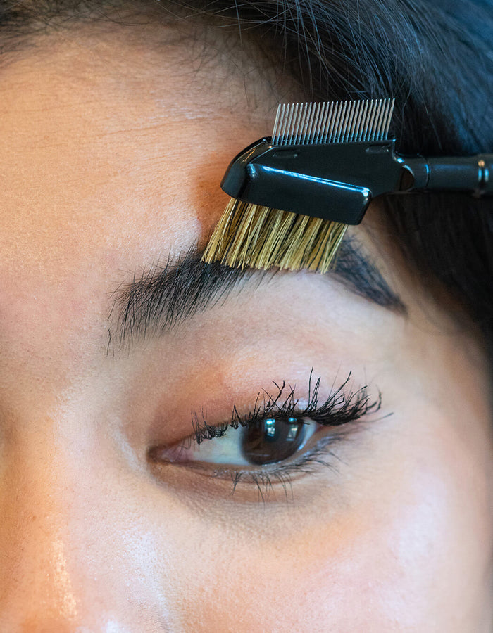Nahaufnahme einer Person, die ihre Augenbrauen mit dem RevitaLash® Cosmetics Lash & Brow Styler, einem doppelseitigen Bürstchen und Kamm, pflegt.