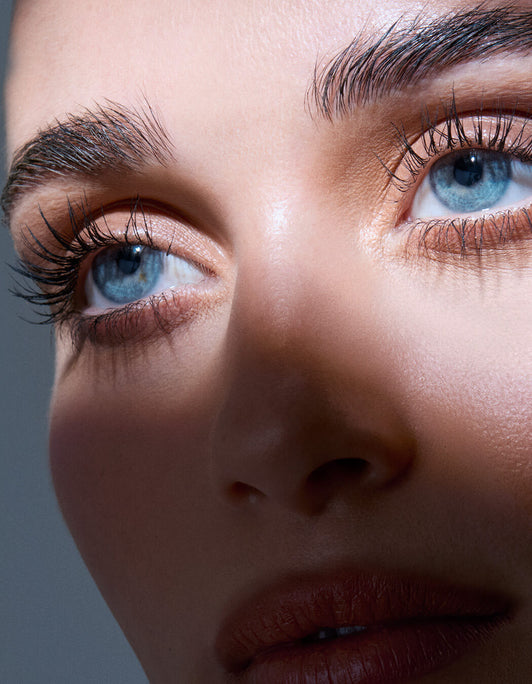 Nahaufnahme des Gesichts einer Person mit blauen Augen und langen Wimpern, die mit dem RevitaLash® Cosmetics Lash & Brow Styler gestylt wurden, und natürlicher Haut in weichem Licht.