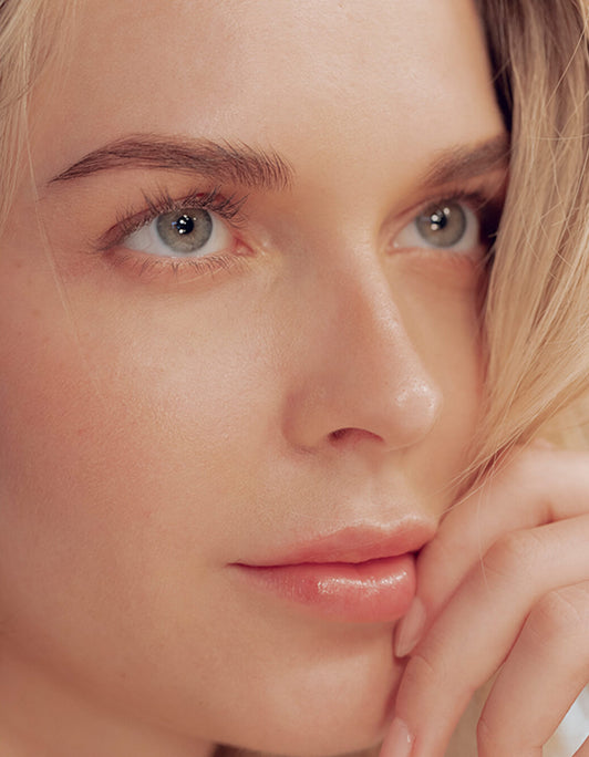 Nahaufnahme einer Frau mit reiner Haut, blauen Augen und blondem Haar, die die Brow Refresh Collection – RevitaBrow Advanced Spring 2025 von RevitaLash® Cosmetics präsentiert.