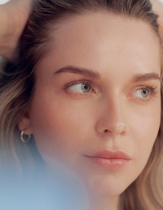 Eine Frau mit reiner Haut und kleinen Creolen berührt sanft ihr Haar, nachdem sie RevitaLash® Cosmetics Micellar Water Lash Wash verwendet hat.