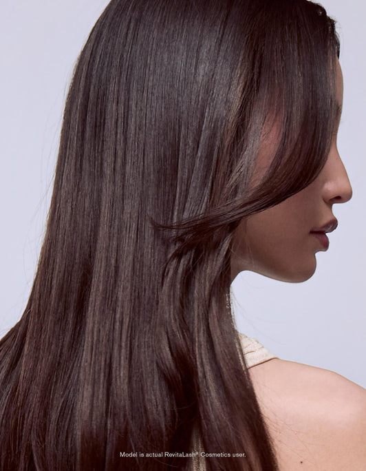 Eine Frau mit langem, glattem, glänzendem dunklem Haar - dank der Leave-In Hair Mask & Conditioner von RevitaLash Germany - im Profil vor einem hellen Hintergrund.