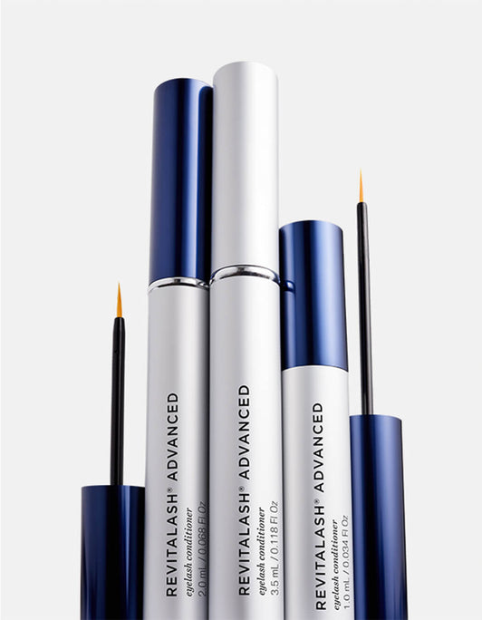 Drei silberne Tuben RevitaLash® Cosmetics RevitaLash® Advanced Eyelash Conditioner, zwei davon mit geöffneten und ausgestellten Stäbchen mit blauen Kappen.