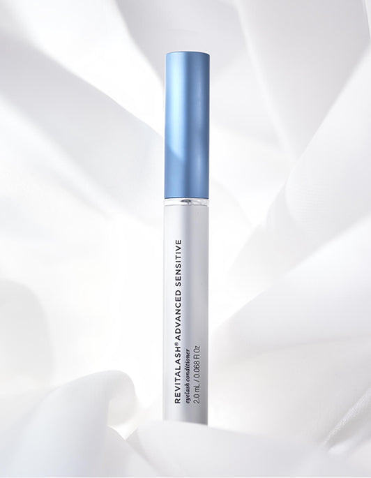 Eine Tube RevitaLash® Cosmetics RevitaLash® Advanced Sensitive Wimpernserum mit blauer Kappe vor einem weichen weißen Stoff.