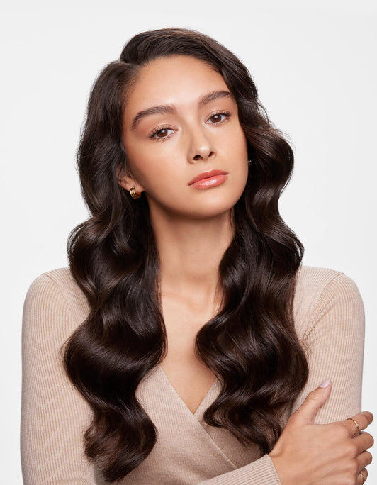 Frau mit langem, welligem, dunklem Haar und neutralem Gesichtsausdruck präsentiert gesund-aussehendes Haar erzielt mit RevitaLash® Cosmetics Thickening Shampoo.