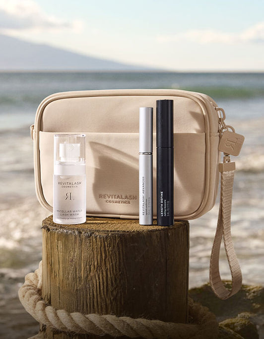 Die Strength & Define Collection – RevitaLash® Advanced von RevitaLash® Cosmetics wird auf einem Holzstamm am Strand präsentiert.