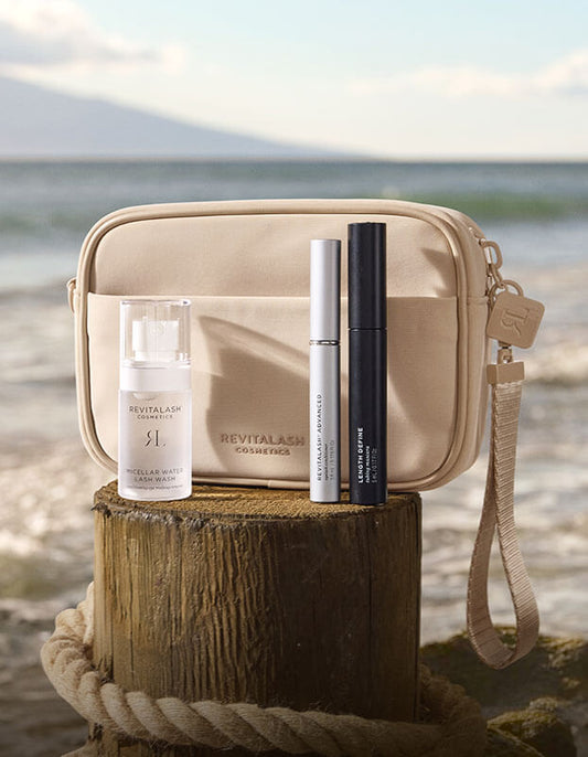 Die Strength & Define Collection – RevitaLash® Advanced von RevitaLash® Cosmetics wird auf einem Holzstamm am Strand präsentiert.