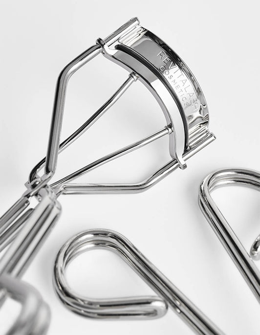 Nahaufnahme der silbernen Signature Eyelash Curler Wimpernzange von RevitaLash® Cosmetics auf weißer Oberfläche.