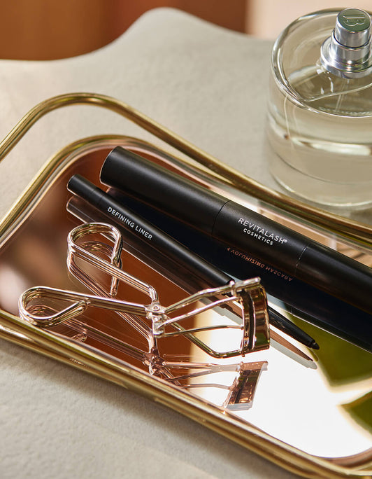 Auf einem goldenen Tablett werden auf  die RevitaLash® Cosmetics Signature Eyelash Curler, der Definig Liner und das  Double-Ended Volume Mascara Set
präsentiert.