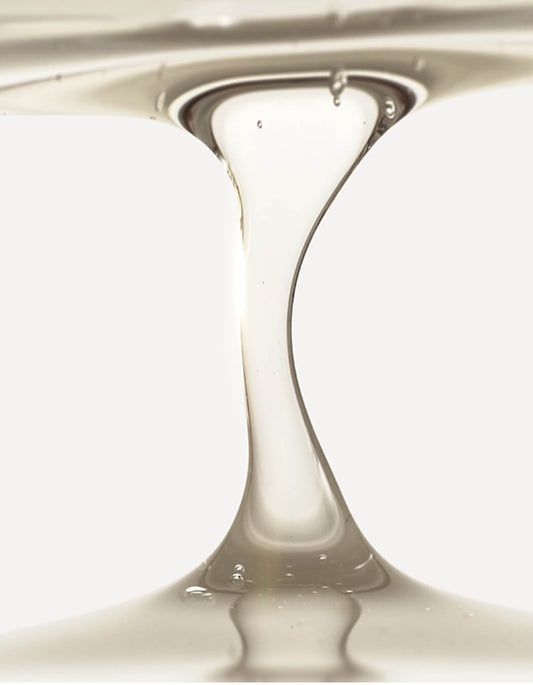 Das RevitaLash® Cosmetics Thickening Shampoo fließt in einem klaren, dickflüssigen Strahl vor einem weißen Hintergrund.