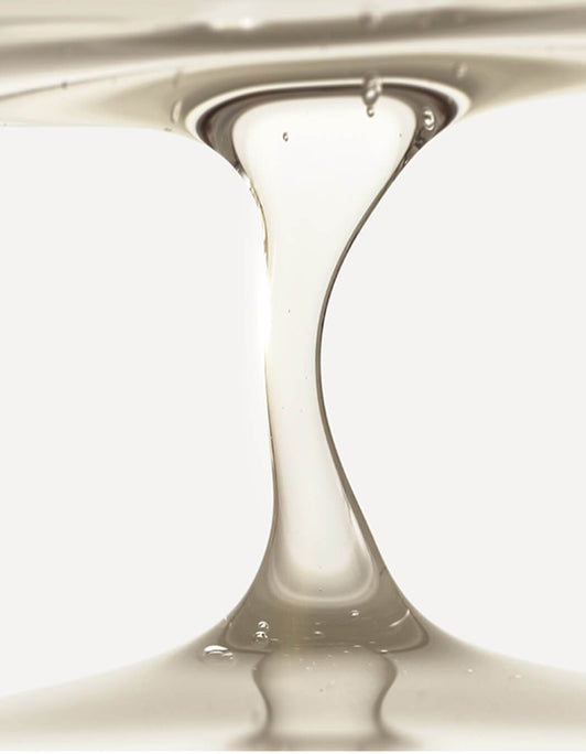 Das RevitaLash® Cosmetics Thickening Shampoo fließt in einem klaren, dickflüssigen Strahl vor einem weißen Hintergrund.