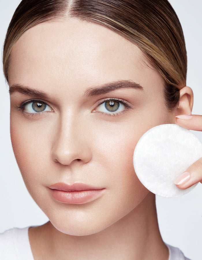 Eine Frau hält ein Wattepad an ihre Wange und präsentiert klare, strahlende Haut und natürliches Make-up.
