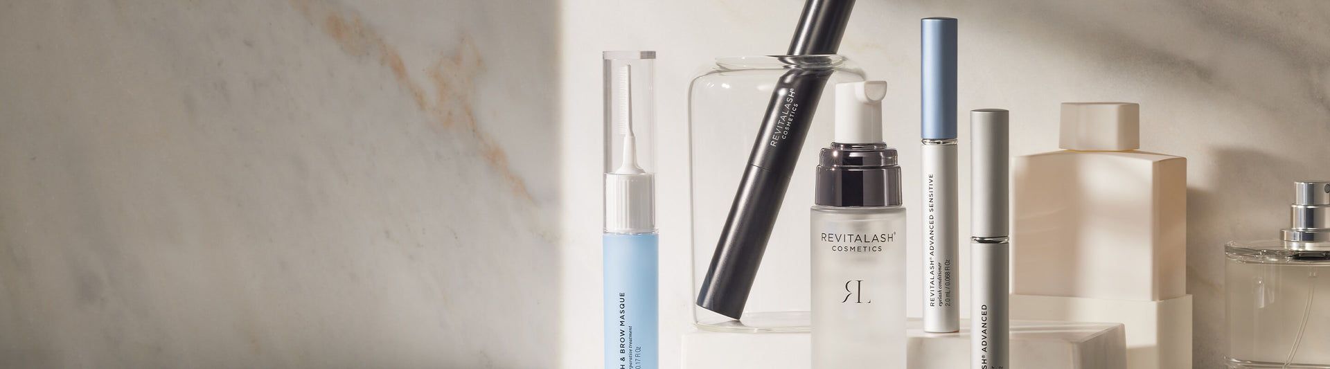 Verschiedene RevitaLash Cosmetics Kosmetikprodukte sind auf einer Marmoroberfläche in sanftem Tageslicht angeordnet.