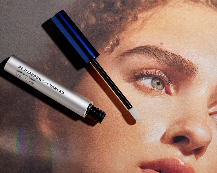 Silberne RevitaBrow Advanced-Tube neben blauer Applikatokappe auf einem Print des Gesichts einer Frau mit definierten Augenbrauen.