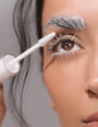 Eine Person trägt mit einem weißen Spiralbürstchen die weiße RevitaLash® Cosmetics Lash & Brow Masque auf ihre Wimpern und Augenbrauen auf.