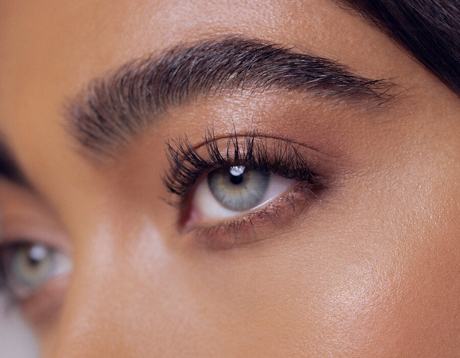 Nahaufnahme der blaugrünen Augen einer Frau mit Fokus den langen Wimpern und gepflegten Augenbrauen.