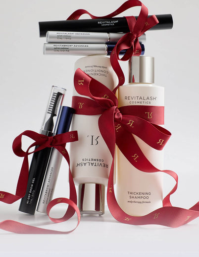 Haar- und Wimpernprodukte von RevitaLash Cosmetics mit roten Schleifen als Geschenke verpackt auf weißem Hintergrund.