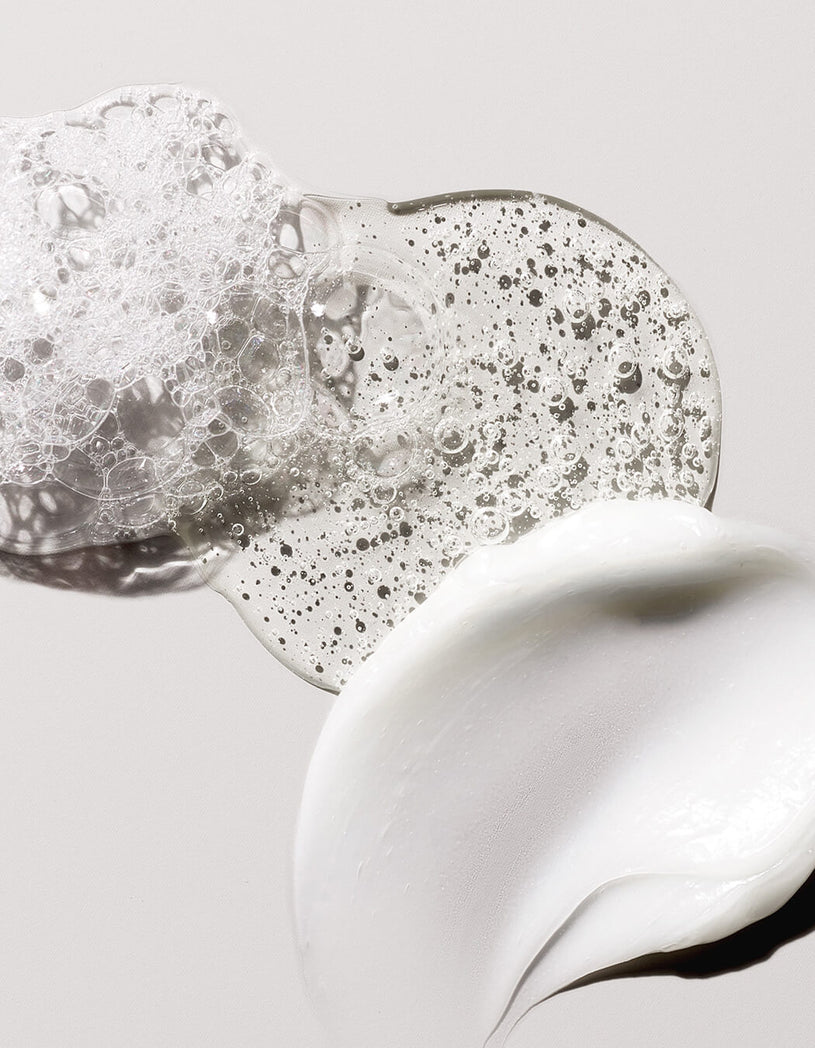 Klares Gel, weiße cremige Lotion und Schaumtexturen verteilen sich auf einer glatten, hellen Oberfläche.