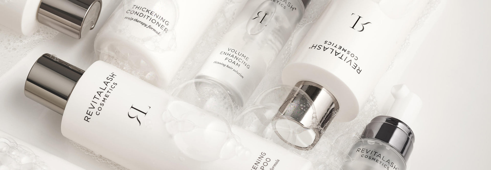 Haarpflegeprodukte von RevitaLash Cosmetics, angeordnet auf einer weißen, seifigen Oberfläche.