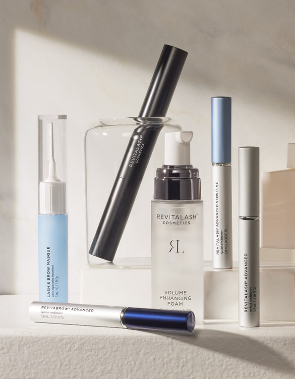 Mehrere Kosmetikprodukte von RevitaLash Cosmetics, angeordnet auf einer beigen Oberfläche mit sanfter Beleuchtung.