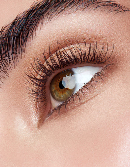 Nahaufnahme eines haselnussbraunen Auges mit langen Wimpern und gepflegten Augenbrauen auf glatter, heller Haut.