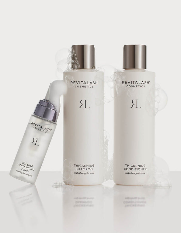 Drei weiße RevitaLash-Haarpflegeflaschen mit Blasen auf weißem Hintergrund.