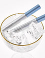 Zwei silber-blaue Tuben RevitaLash® Advanced Sensitive Eyelash Conditioner liegen in einem Glas mit Eiswürfeln und Goldrand.