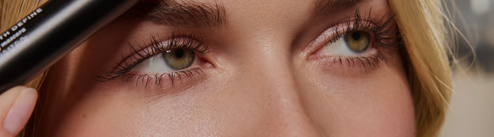 Nahaufnahme der Augen einer Frau; sie hält eine Length Define Mascara nahe den Wimpern, die lang, getrennt und betont wirken.