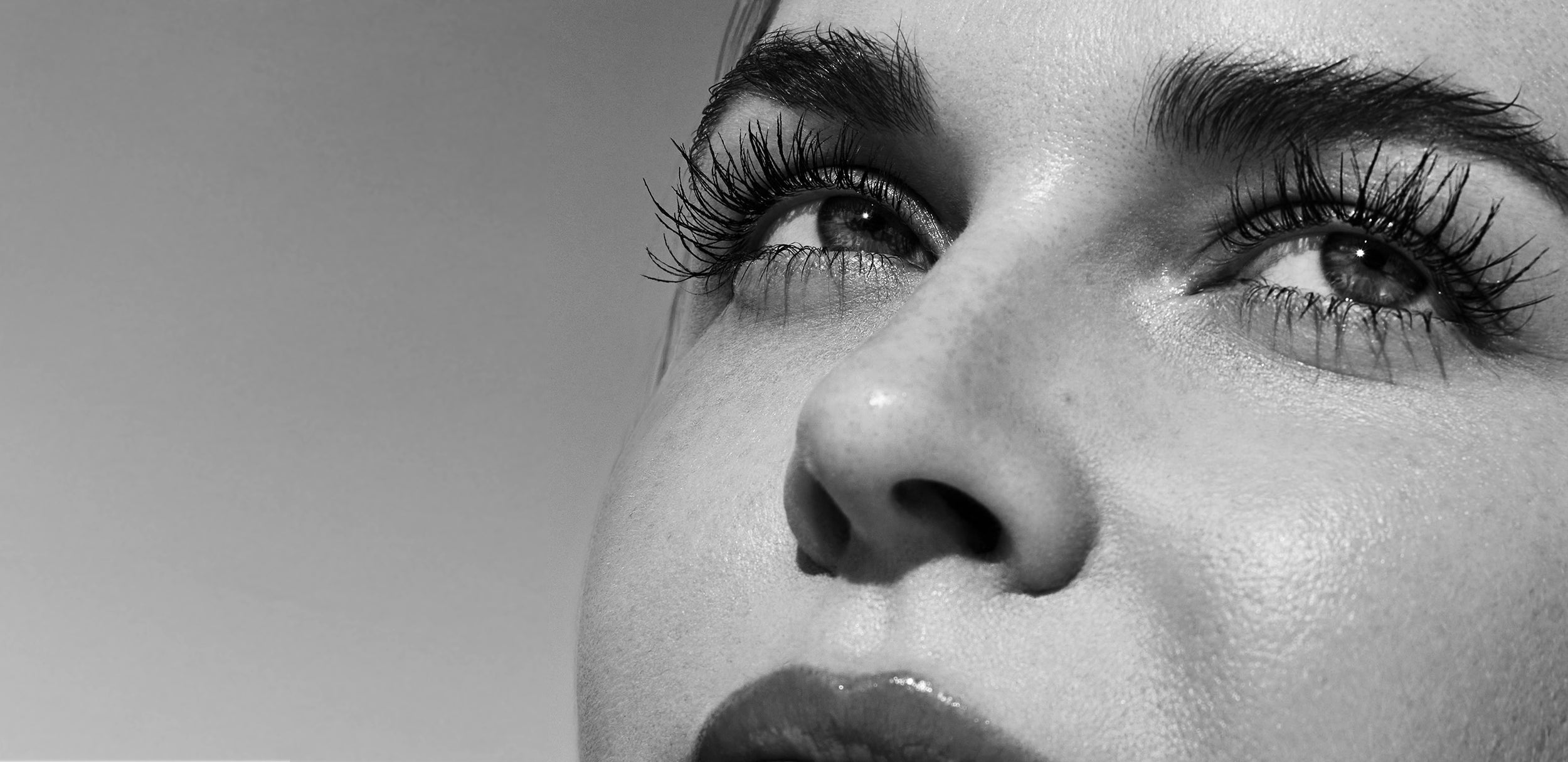 Schwarzweiß-Nahaufnahme eines Gesichts: Fokus auf Augen mit langen Wimpern, Blick nach oben, Hautstruktur und Nase deutlich sichtbar.