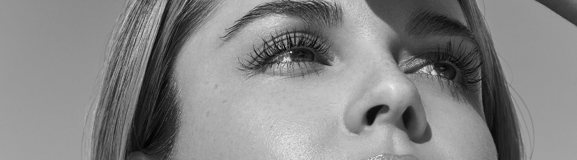 Schwarzweiß-Nahaufnahme eines Gesichts: Fokus auf Augen mit langen Wimpern, Blick nach oben, Hautstruktur und Nase deutlich sichtbar.