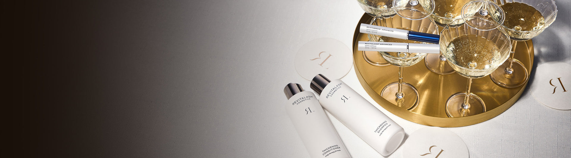 RevitaLash Haarpflegeprodukte neben Sektgläsern auf goldenem Tablett, elegant arrangiert auf hellem Tisch.