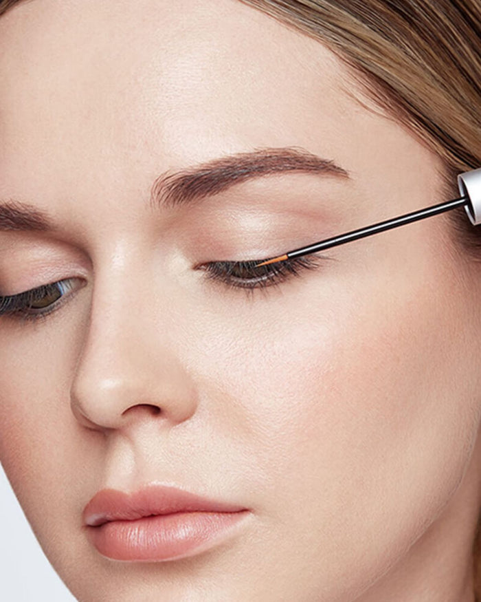 Eine Frau trägt mit einem Pinselapplikator RevitaLash Advanced Eyelash Conditioner auf ihren Wimpernkranz auf.